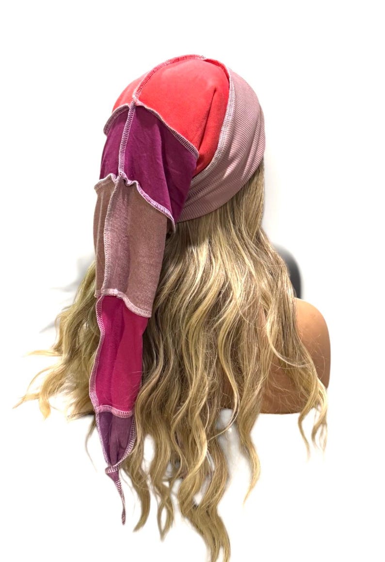 May include: A patchwork head covering featuring a ribbed mauve band and a long, pointed tail constructed from multiple fabric panels in shades of bright red, deep magenta, muted brown, and dark purple, all joined with visible light-colored stitching.