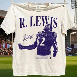 May include: A cream-colored short-sleeve t-shirt featuring a purple graphic print of a football player wearing jersey number 52. The text R. LEWIS is printed in large purple letters above the player, accompanied by a signature graphic on the left.