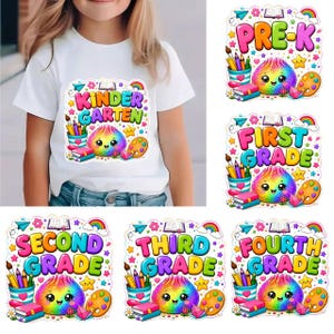 Könnte beinhalten: Ein weißes T-Shirt mit einem bunten Grafikdruck mit den Texten KINDERGARTEN, PRE-K, FIRST GRADE, SECOND GRADE, THIRD GRADE und FOURTH GRADE, begleitet von Illustrationen eines Regenbogens, Büchern, Stiften und einer lächelnden Regenbogenkreatur.