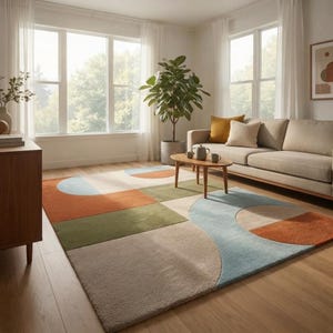 Può includere: Un tappeto rettangolare con un motivo geometrico di grandi semicerchi e rettangoli in tonalità tenui di arancione terracotta, verde salvia, azzurro e beige. Il tappeto è posizionato su un pavimento in legno chiaro in una stanza luminosa.
