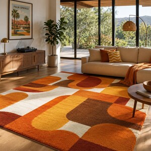 May include: A rectangular area rug featuring a geometric pattern of overlapping rounded shapes in shades of burnt orange, mustard yellow, dark brown, and cream. The rug has a thick, textured pile and covers a large portion of the wooden floor.