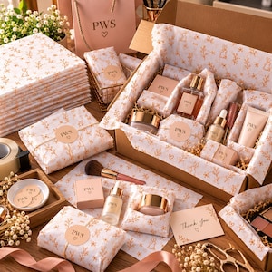 Puede incluir: Un set de regalo con productos de cuidado de la piel, incluyendo frascos de vidrio con goteros, tarros con tapas doradas y un tubo, envueltos en papel de seda blanco con un patrón floral y de conejos en dorado. Marcados con PWS y un corazón.