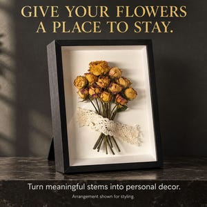 Puede incluir: Un marco de caja negra que contiene un ramo de rosas secas amarillas y rosas atadas con una cinta de encaje blanco sobre un fondo blanco. El texto dice: GIVE YOUR FLOWERS A PLACE TO STAY. Turn meaningful stems into personal decor.