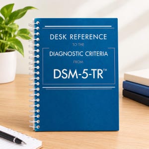 May include: A blue spiral-bound book titled Desk Reference to the Diagnostic Criteria from DSM-5-TR. The cover features white text with horizontal lines above and below the title, and a white metal coil binding along the left side of the book.