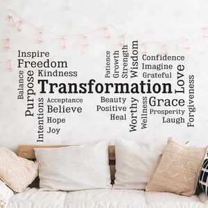 Könnte beinhalten: Ein lichtdurchfluteter Raum mit einem Futon-Sofa aus Holz, das mit Kissen und einem gewebten Überwurf geschmückt ist. Links steht ein großer Kaktus in einem Papierbehälter. Das Wort "Transformation" ist an der Wand zu sehen, umgeben von verwandten Wörtern.