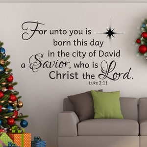 May include: A Christmas-themed living room with a decorated Christmas tree, a couch with pillows, a wreath, and a wall decal with the Bible verse "For unto you is born this day in the city of David a Savior, who is Christ the Lord. Luke 2:11"