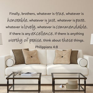 May include: A living room scene featuring a white sofa with decorative pillows and two glass-topped coffee tables. The wall displays a quote from Philippians 4:8 in black script: "Finally, brothers, whatever is true..." Two lamps flank the sofa.
