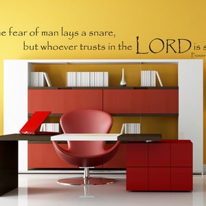 May include: A motivational quote on a yellow wall in a modern office setting. The quote reads: "The fear of man lays a snare, but whoever trusts in the LORD is safe. Proverbs 29:25".