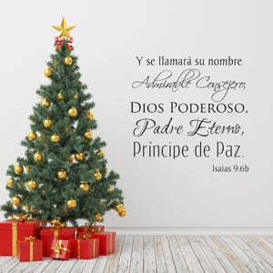 May include: A decorated Christmas tree with gold ornaments and a gold star topper, surrounded by red gift boxes tied with gold ribbons. Text in Spanish on the wall reads "Y se llamará su nombre..." (Isaiah 9:6b).
