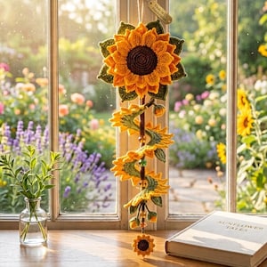 May include: A crocheted sunflower wall hanging featuring a large central bloom with yellow petals and a dark brown center, connected to a spiraling vine of smaller sunflower motifs and green leaves, accented with beads and a small wooden tag.