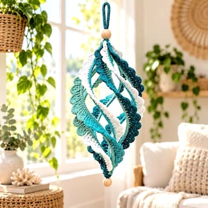 May include: A hanging spiral ornament crafted from teal and white crocheted yarn, featuring a scalloped edge design. The structure is suspended by a matching teal yarn loop and accented with two smooth, round wooden beads at the top and bottom.