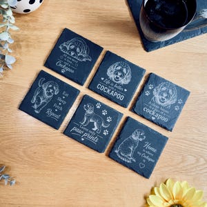 May include: A set of six square black slate coasters, each featuring a unique white engraved illustration of a Cockapoo dog and text. The phrases include All you need is love and a Cockapoo, Life is better with a Cockapoo, Eat Sleep Fetch Repeat, Leave only paw prints, A clean house is a sign of a Cockapoo, and Home is where my Cockapoo is.