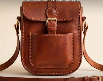 May include: A brown leather saddle bag featuring a front pocket, a flap closure with a brass buckle, and an adjustable shoulder strap. The text "Leather Saddle Bag" is printed at the top, and "by RumBloom" is at the bottom left.