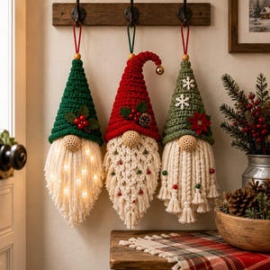May include: Three hanging gnome ornaments with crocheted hats in green and red. The left gnome has a light-up beard, the center has a macrame beard with small beads, and the right has a braided beard with small ornaments and a poinsettia accent.
