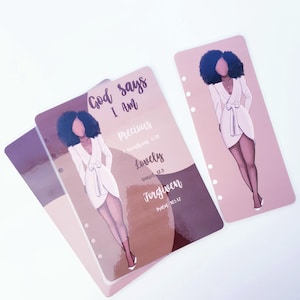 May include: Planner inserts with illustrations of a woman in a white dress. The inserts have the text "God says I Am" and the words "Precious," "Lovely," and "Forgiven." The background is a mix of brown and pink.