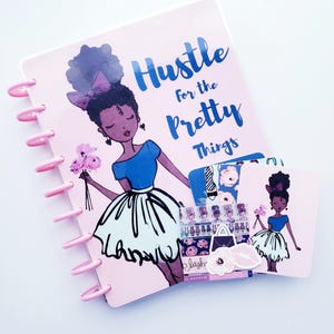 May include: A pink planner with a cartoon illustration of a woman holding flowers, with the text "Hustle for the Pretty Things" in blue. The planner has pink rings and is accompanied by matching cards and stickers.