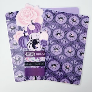 May include: A planner with a purple spider web design, featuring decorative elements like pumpkins, roses, and washi tape. The washi tape has the words "Relax" and "Breathe" printed on it. The planner is open, revealing the inside pages.