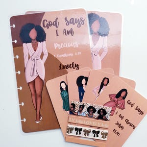 May include: A collection of stationery items featuring illustrations of women in various outfits. The items include planner inserts and cards with inspirational text like "God says I Am Precious" and "I Am Chosen". A decorative ribbon with bows is also included.