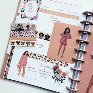 May include: A planner with a pink cover and gold rings, open to a spread with stickers, washi tape, and handwritten notes. The stickers feature illustrations of women in pink dresses. The washi tape has a leopard print and bow design.