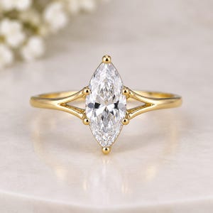 Peut inclure: Une bague en or avec une pierre précieuse transparente taille marquise sertie au centre. L'anneau présente un design à tige fendue qui s'affine vers la pierre, maintenue par quatre petites griffes. Le métal a une finition polie et brillante.