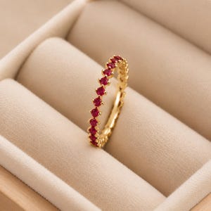 Op de afbeelding: Een gouden ring met een doorlopende rij kleine, ronde, felrode edelstenen langs de buitenrand. De ring staat rechtop, waardoor de gelijkmatige ronde slijpvorm van de stenen en de gepolijste gouden zetting goed zichtbaar zijn.