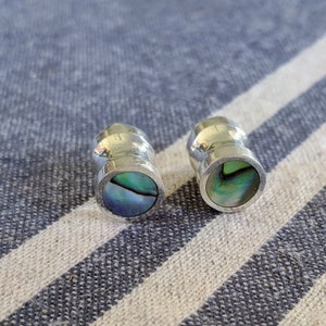 May include: A pair of silver earrings with abalone shell insets. The earrings are round and have a smooth, polished finish.