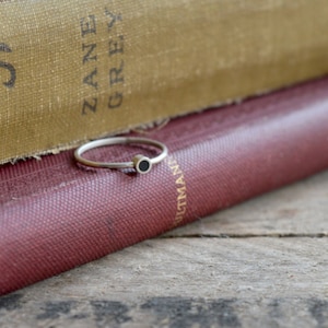 May include: A thin gold band ring with a small black circle in the center. The ring is resting on top of two stacked books. The top book has the text "ZANE GREY" printed on the cover.