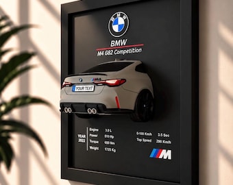 Könnte beinhalten: Ein schwarzer Wandrahmen mit einem 3D-Modell des Hecks eines grauen BMW M4 G82 Competition. Das Display enthält das BMW-Logo, technische Daten wie 3.0 L Motor, 510 PS, 650 Nm, 1725 kg, 0-100 km/h in 3.5 Sek, 290 km/h Höchstgeschwindigkeit und das M-Logo.