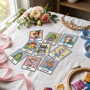 May include: A collection of nine rectangular cards featuring cartoon character illustrations labelled Mulan, Rapunzel, Jasmine, Ariel, Pocahontas, Elsa, Tiana, Moana, and Cinderella. The cards are arranged on a white fabric surface with flowers, a gold tiara, and ribbons.