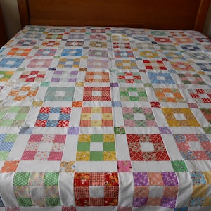 May include: A colorful patchwork quilt with a white background and squares of various floral patterns in shades of pink, blue, green, yellow, and red.