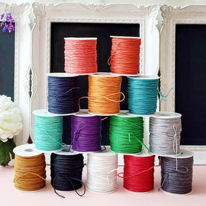 Peut inclure: Une collection de quatorze bobines de cordon disposées en forme de pyramide. Les bobines présentent une variété de couleurs, notamment le rouge, l'orange, le jaune, le vert, le bleu, le violet, le blanc, le gris et le noir. Chaque bobine est enroulée.