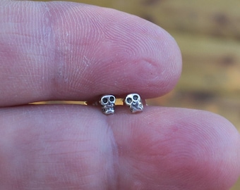 May include: A pair of small silver skull earrings. The skulls are detailed and have black eyes.