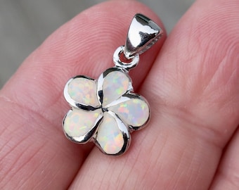 Può includere: Un ciondolo d'argento con un fiore di opale bianco dal design delicato. Il fiore ha cinque petali e un centro leggermente rialzato. Il ciondolo è perfetto per aggiungere un tocco di eleganza a qualsiasi outfit.