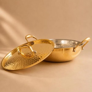 May include: A round, hammered gold-tone metal cooking pot with two side handles and a matching lid. The exterior of the pot and the lid feature a textured, dimpled surface, while the interior of the pot has a smooth, metallic silver-tone finish.