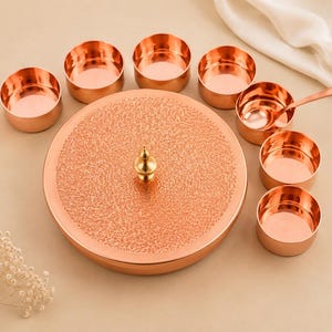 Könnte beinhalten: Eine runde Gewürzdose aus Kupfer mit strukturiertem Deckel und zentralem Messingknauf, begleitet von sieben kleinen passenden Kupferschalen und einem Kupferlöffel. Das Set zeichnet sich durch ein poliertes Metallfinish und ein kreisförmiges Design aus.