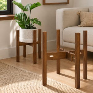 May include: Two dark brown wooden plant stands with a cross-jointed base design. One stand holds a light gray speckled ceramic pot containing a green monstera plant with large, split leaves. The stands feature four vertical legs each.