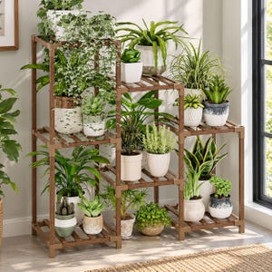 May include: A multi-tiered brown wooden plant stand featuring a modular frame with square connectors. The stand holds numerous potted plants of various sizes, including trailing ivy, snake plants, succulents, and leafy green foliage in ceramic pots.