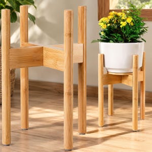 Peut inclure: Deux supports pour plantes en bambou de couleur claire avec une base en forme de croix et quatre pieds cylindriques. L'un est vide, tandis que l'autre soutient un pot en céramique blanche contenant une plante verte aux petites fleurs jaunes.