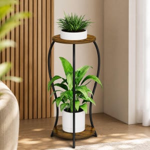 May include: A two-tier plant stand featuring a black metal frame with curved supports and two circular shelves with a brown wood-grain finish. The stand holds a white pot with a green plant on the top shelf and a white pot with a green plant on the bottom shelf.