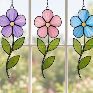 May include: Three stained glass flower suncatchers hanging by chains. Each flower has five petals in purple, pink, or blue, with a yellow center. Each stem features two green leaves. The pieces are outlined in black metal, creating a floral design.