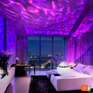 Può includere: Un proiettore di luce sferico bianco con una cupola sfaccettata posizionato su un letto in una stanza illuminata da motivi luminosi a nebulosa viola e rosa proiettati su soffitto e pareti, con lo skyline della città visibile dalle finestre.