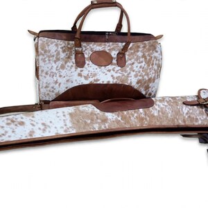 May include: A brown and white cowhide leather duffel bag with two top handles and a matching long, narrow, rectangular cowhide leather case with a flap closure, both featuring brown leather trim and metallic hardware accents.