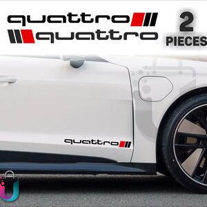 Peut inclure: Un ensemble de deux autocollants en vinyle noir et rouge affichant le mot quattro dans une police sans empattement minuscule, appliqués sur le côté d'une voiture blanche. Le design inclut un rectangle rouge et deux barres verticales noires.