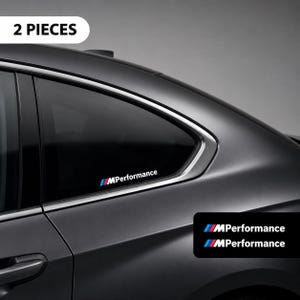 Op de afbeelding: Een set van twee MPerformance-stickers met de tekst MPerformance in het wit en een logo met schuine strepen in blauw, lichtblauw en rood. De stickers zijn afgebeeld op het achterste zijraam van een donkergrijze auto en als los paar.