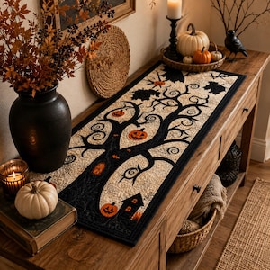 May include: A rectangular table runner featuring a quilted design with a black tree silhouette, orange jack-o'-lanterns, and a small house on a cream-colored background. The runner has a black border and intricate stitching throughout the fabric.