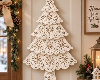 Puede incluir: Una decoración navideña de pared en forma de árbol de color crema, hecha de capas de tela troquelada con intrincados patrones florales y de copos de nieve. El árbol presenta un diseño de borde festoneado y un tronco pequeño y simple.