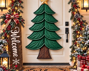 May include: A quilted green fabric Christmas tree wall hanging with a gold star topper, displayed on a white door. Beside it, a wooden sign reads Welcome with a snowflake icon, and a brown coir doormat features the text Welcome.