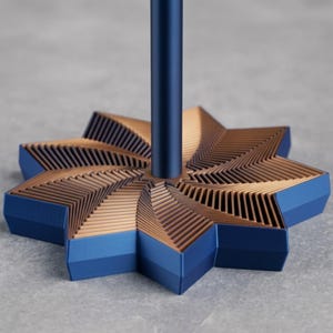 May include: A vertical blue cylindrical rod attached to the center of a star-shaped base. The base features a layered, geometric design with alternating blue outer edges and copper-colored inner fins that create a spiraling, textured pattern.