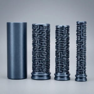 May include: Four cylindrical objects in a metallic dark gray finish. One cylinder has a smooth, solid surface, while the other three feature intricate, raised maze-like patterns of varying widths, each with a distinct base ring detail.