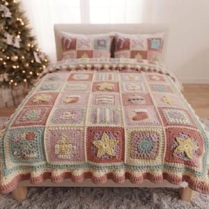 May include: A crochet blanket and two matching pillows featuring a grid of squares in muted tones of pink, blue, and cream. Each square displays textured holiday-themed motifs including stars, stockings, and trees, finished with a ruffled edge.